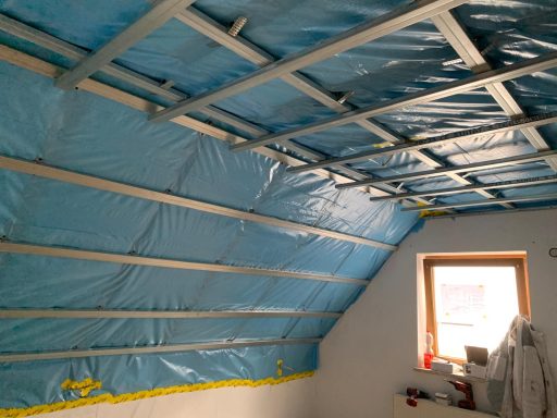 Raum mit schrägem Dach, blauer Folie und Holzrahmenkonstruktion.